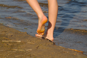 The child walks along the sandy shore of the pond. Feet close up.