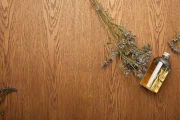 top view of transparent bottle with organic beauty product near dried herbs on wooden background