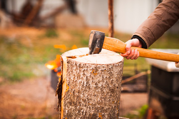 Man chops wood with an ax. Bonfire background. Close up.