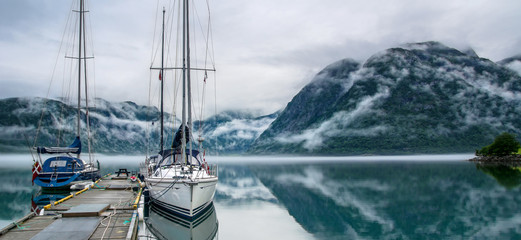 Amazing nature landscape view of lake surrounded by foggy mountains. Sailing vessels or ships. Nature lake. Forest natural. Location: Scandinavian Mountains, Norway. Artistic picture. Panorama