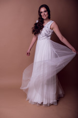 Fototapeta na wymiar Beautiful young girl in a flying white dress. Flowing fabric. bride in white dress on beige background. gorgeous brunette on a studio background. Isolate