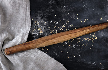 very old wooden rolling pin on a black background, near a gray linen towel