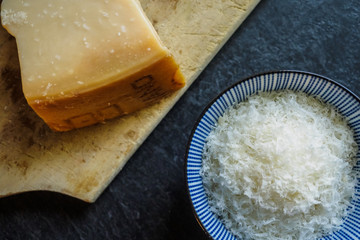 Grated parmesan cheese in a bowl on black background, italian food.