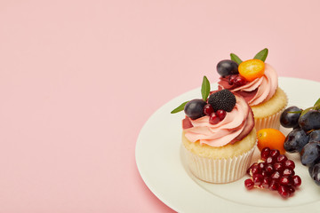 sweet cupcakes with berries and fruits on plate on pink surface