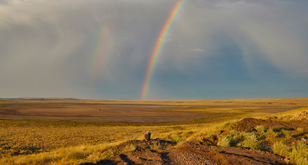 Spectacular landscape with a colorful rainbow in stormy sky, yellow dry grass and bright blue sky....
