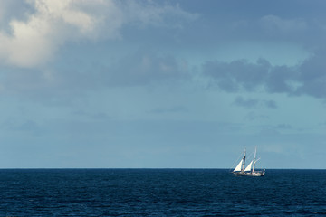 A large blue sailing boat with white sails, making it's way up the east coast of Australia on the Pacific Ocean; deep blue sea and a lightly cloudy blue sky.
