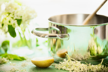 Close up of elderflowers, lemon and sugar on kitchen table with cooking pot. Homemade elderflower...
