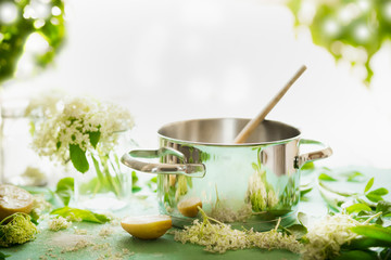 Elder flowers syrup cooking preparation. Pot with wooden spoon on kitchen table with sugar, lemon and elderflowers. Healthy seasonal natural food concept. Copy space for your recipes