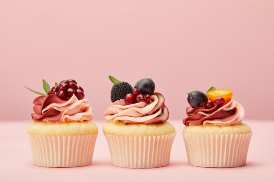 sweet cupcakes with fruits and berries on pink surface