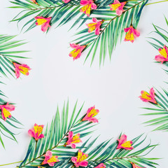 Fototapeta premium Tropical background with palm leaves and exotic flowers on white background, top view. Frame. Flat lay. Copy space for your design