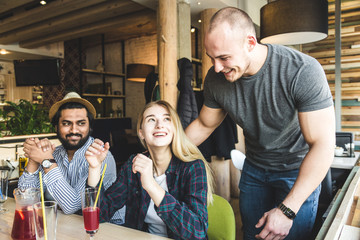 a group of young cheerful friends are sitting in a cafe, eating, drinking drinks, take selfies and take pictures. meeting, handshake and hugs