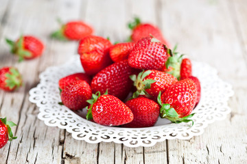 Fresh red strawberries on white plate on rustic wooden background.