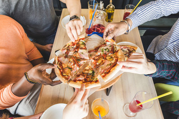 A company of multicultural  young people in a cafe eating pizza, drinking cocktails, having fun