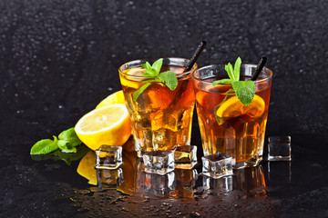 Two glasses with cold traditional iced tea with lemon, mint leaves and ice cubes.