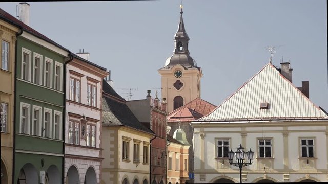 Medieval Renaissance square with stone tower and clock. View to row of houses with colorful old facades and blue sky. Age-old gas lamp and arcades. Static sunny day shot, color corrected footage