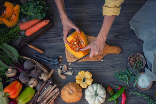 Woman chopped pumpkin over a rustic table filled with delicious and healthy vegan food. Top view. Toned image.