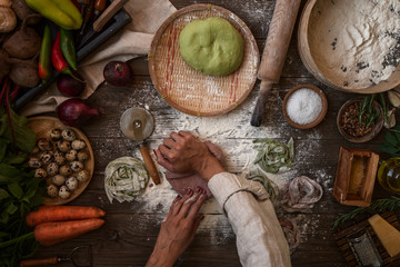 Making homemade pasta linguine on rustic kitchen table with flour, rolling pin and vegetables. Rustic style, toned image.