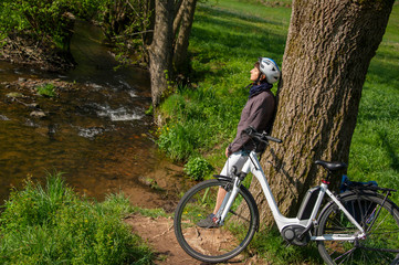 Fototapeta na wymiar Ausflug mit Elektro Fahrrad, Radfahrerin mach Pause an schöner Bachlandschaft