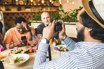 Group of young cheerful friends are sitting in a cafe, eating, drinking drinks. Friends take selfies and take pictures.