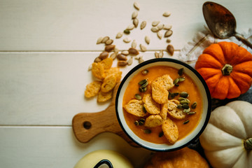 Autumn Halloween or thanksgiving day table setting. Pumpkins, spices, bowl vegetable soup and vintage cutlery on wooden table. Thanksgiving background mock up. Top view, toned image.
