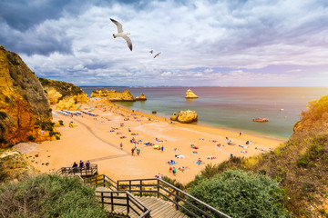 Wooden walkway to famous Praia Dona Ana beach with turquoise sea water and cliffs, flying seagulls...