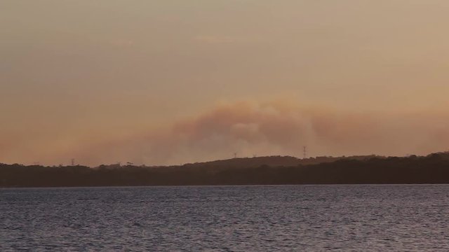 Bushfire season. Large plumes of smoke from a large bushfire or wildfire near a body of water. Best footage for emergency services and summer warnings to evacuate, a call to action of the firefighters