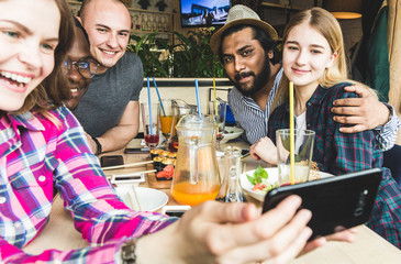 Group of young cheerful friends are sitting in a cafe, eating, drinking drinks. Friends take selfies and take pictures.