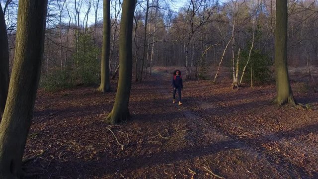 4K Aerial drone clip of teenage young woman hiking with red backpack in forest woodland 