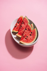 Fresh sliced watermelon in white dish on pink background.
