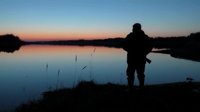 Hunter with a gun at sunset by the lake. Hunting for waterfowl in the autumn-spring season.