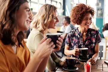 Three Young Female Friends Meeting Sit At Table In Coffee Shop And Talk