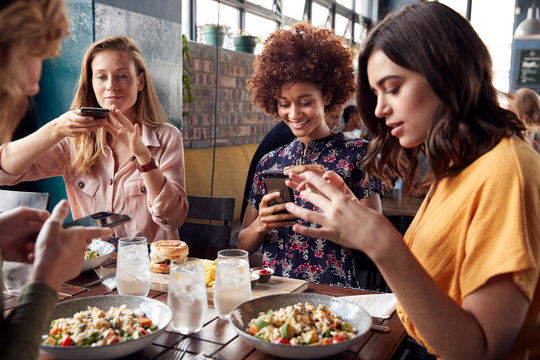 Female Friends In Restaurant Taking Picture Of Food In Restaurant To Post On Social Media