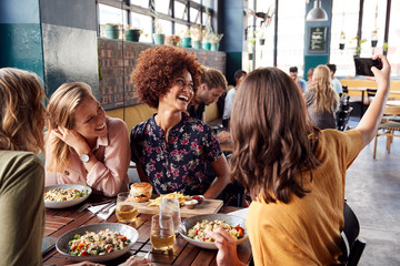 Four Young Female Friends Meeting For Drinks And Food Posing For Selfie In Restaurant