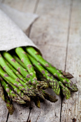 Bunch of fresh raw garden asparagus closeup and linen napkin on rustic wooden table background.
