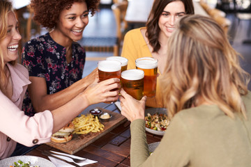 Four Young Female Friends Meeting For Drinks And Food Making A Toast In Restaurant