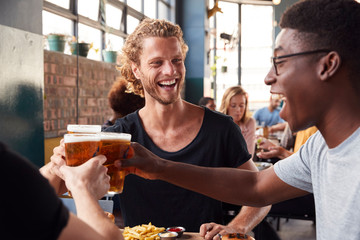 Three Young Male Friends Meeting For Drinks And Food Making A Toast In Restaurant