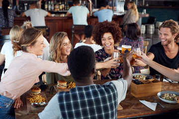 Group Of Young Friends Meeting For Drinks And Food Making A Toast In Restaurant