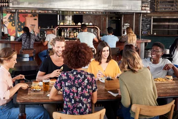 Fotobehang Groep jonge vrienden die elkaar ontmoeten voor drankjes en eten in het restaurant © Monkey Business
