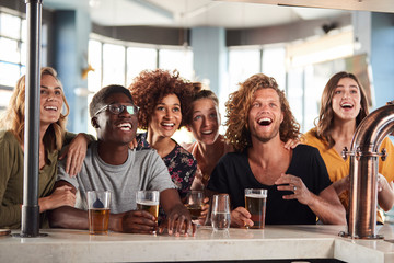 Group Of Male And Female Friends Celebrating Whilst Watching Game On Screen In Sports Bar