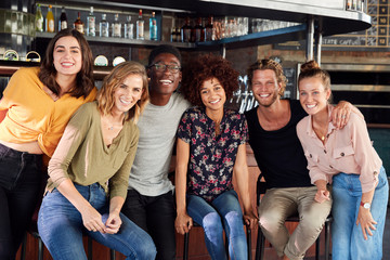 Obraz premium Portrait Of Male And Female Friends Sitting By Counter In Sports Bar