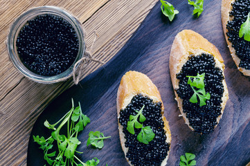 a glass jar of halibut caviar and sandwiches with the caviar and butter decorated with garden cress...