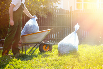Man gardener puts bags of compost in the cart. Green uniform. Light