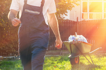 A man in uniform goes for a broom. In the background is a cart with garbage bags. Tint and light