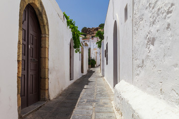 Narrow street in Lindos town on Rhodes island, Dodecanese, Greece. Beautiful scenic old ancient white houses with flowers. Famous tourist destination in South Europe