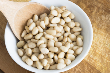 Iberian raw pine nuts in white ceramic bowl with wooden spoon, healthy vegetarian ingredient 