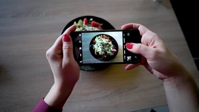 Young woman in a restaurant make photo of food with mobile phone camera. Woman make photo of salad