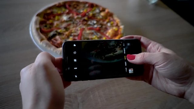 Young woman in a restaurant make photo of food with mobile phone camera. Woman make photo of pizza