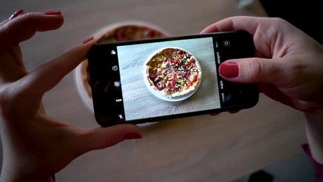 Young woman in a restaurant make photo of food with mobile phone camera