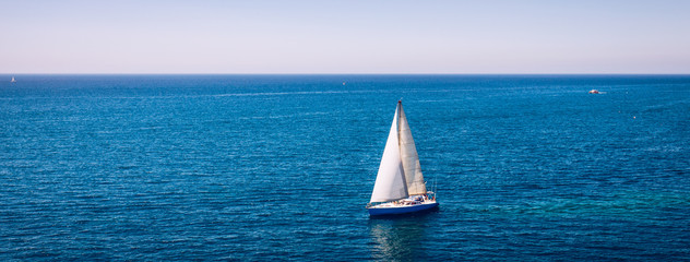 White sail boat isolated in blue sea water. Sailboat in the sea in the sunlight, luxury summer...