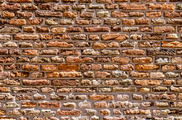 Old masonry wall, relatively clean, with ageing bricks in hues between orange, red and brown